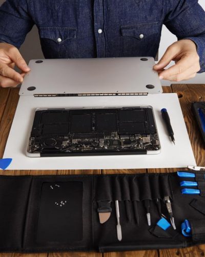 Service man opens backside topcase cover of computer laptop before repairing, cleaning and fixing it with his professional tools from toolkit box near on wooden table front view